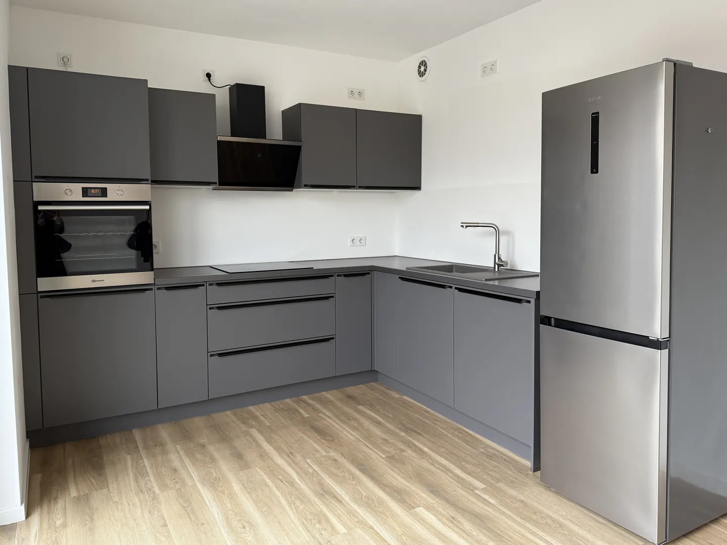 A modern kitchen with gray cabinets, stainless steel appliances, and light wood floors.
