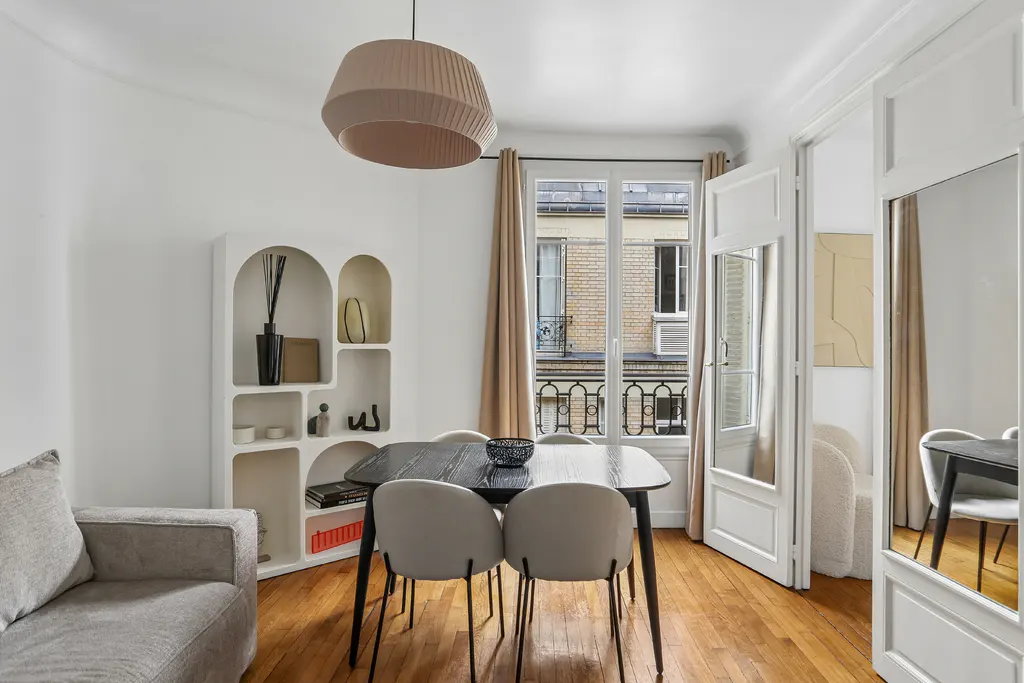 Bright dining area with a black table, four beige chairs, arched shelving, and a large pendant light over hardwood floors.