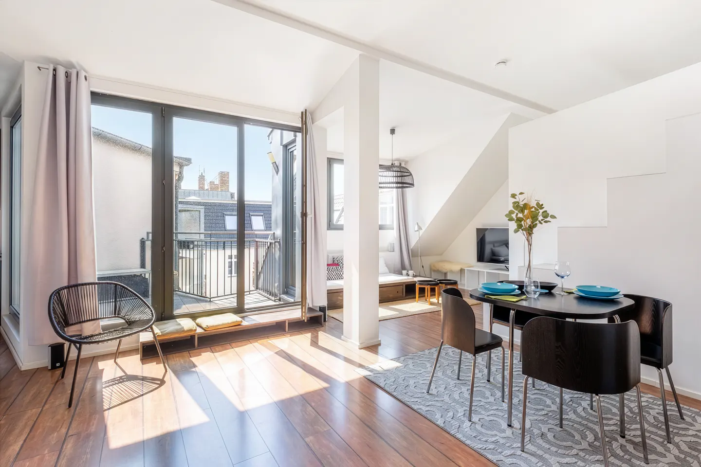Bright, modern apartment interior with wood floors, a black dining table set for four, and a balcony with city views.
