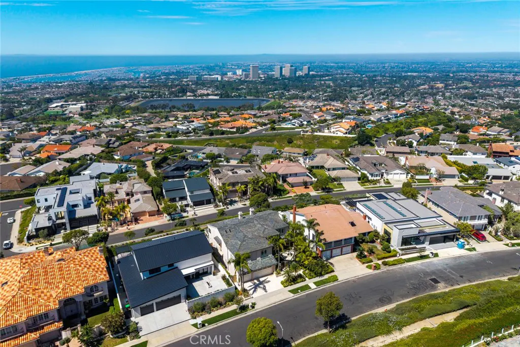 Aerial view of a residential neighborhood with houses, trees, and a distant cityscape under a blue sky.
