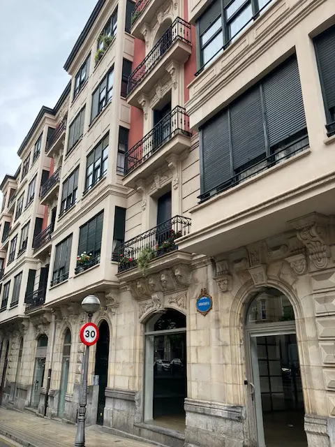 Exterior view of a multi-story building with balconies, arched doorways, and a "30" speed limit sign.