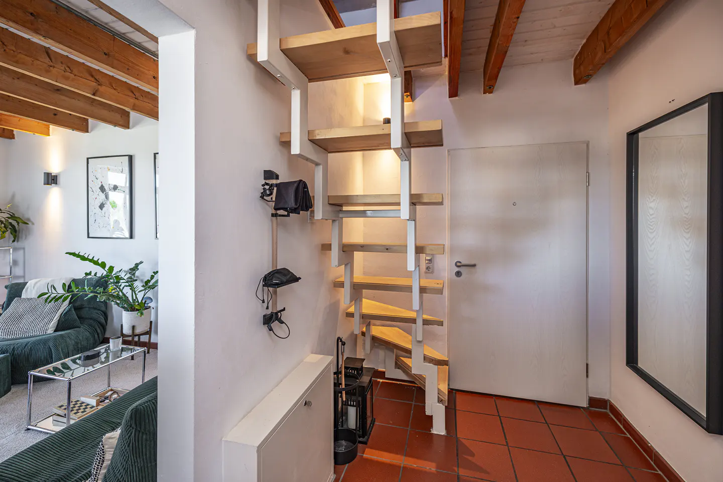 A modern home interior with a wooden staircase, red tile floor, and a glimpse of a green sofa.