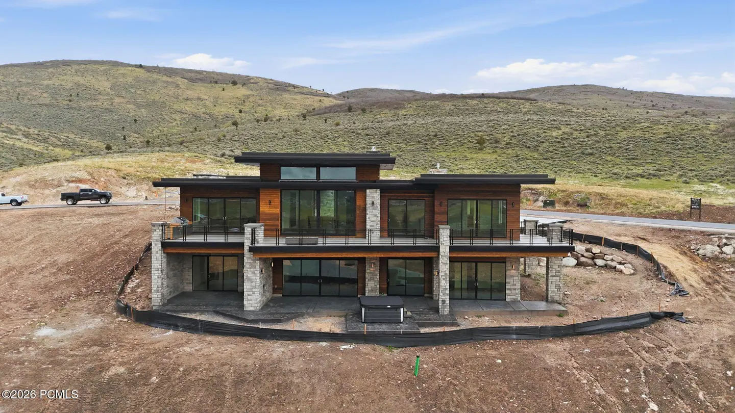 Two-story modern home with wood and stone accents, black trim, and large windows. Balconies overlook a hillside.
