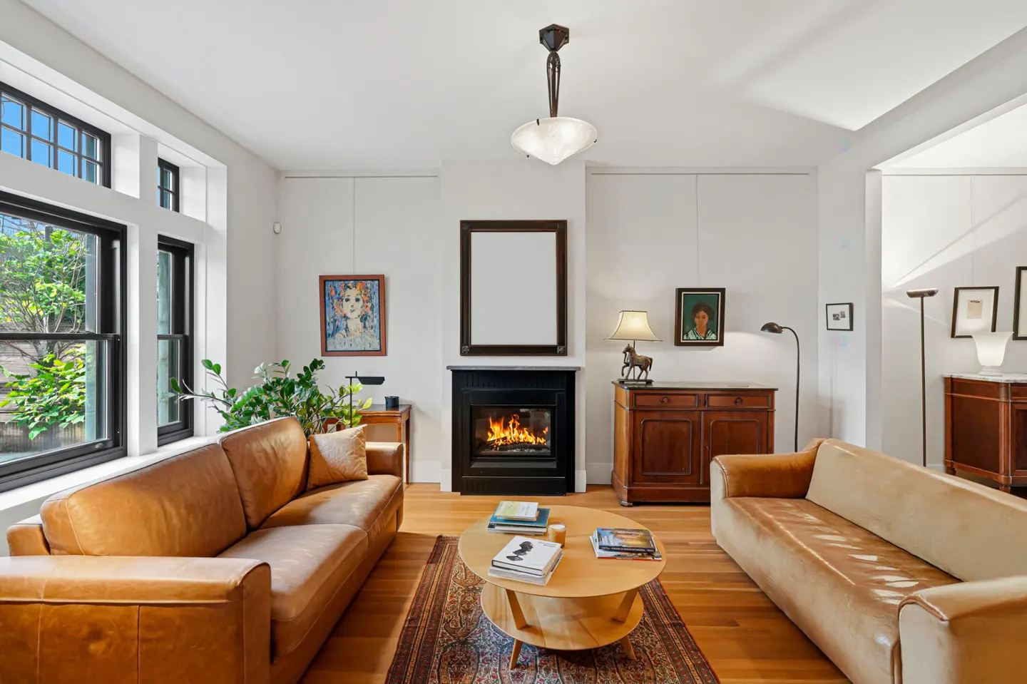 Living room with hardwood floors, two leather sofas, and a black fireplace with a blank picture frame above it.