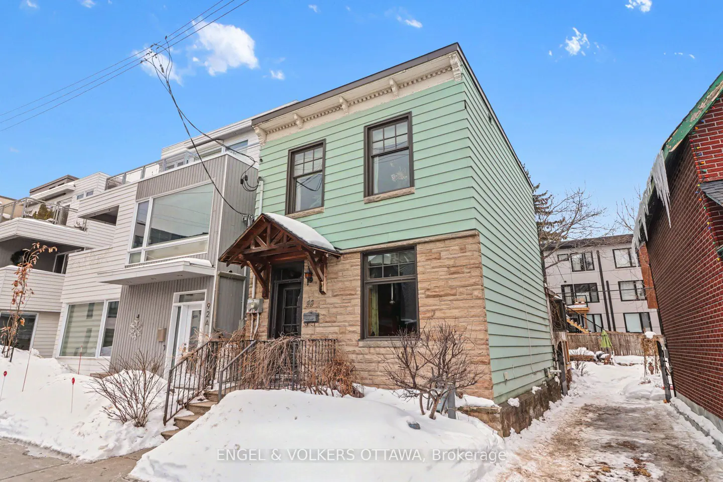 Two-story house with light green siding and stone facade, snow on the ground, and a covered porch.
