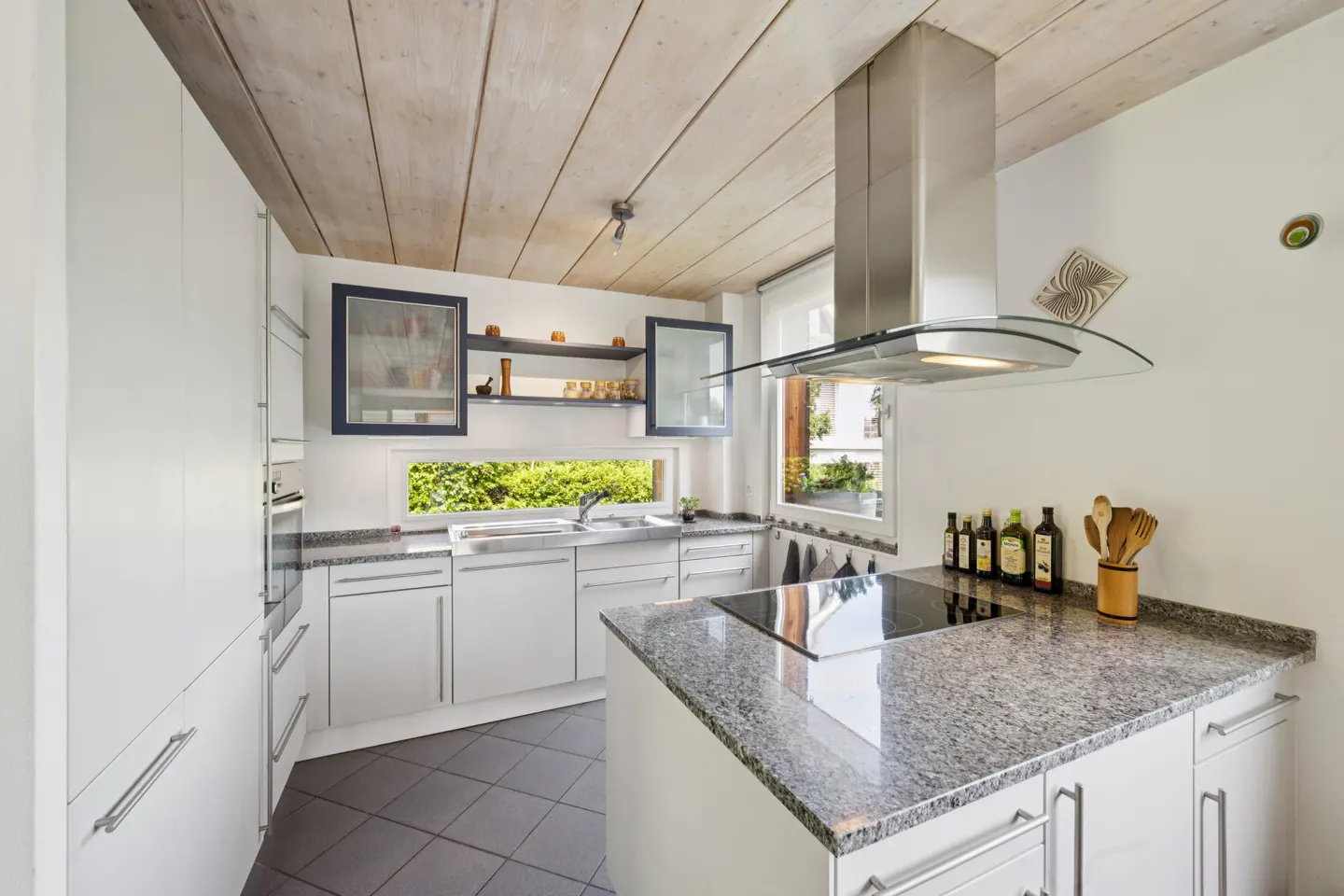 Bright kitchen with white cabinets, granite countertops, and stainless steel hood. A window overlooks green foliage.