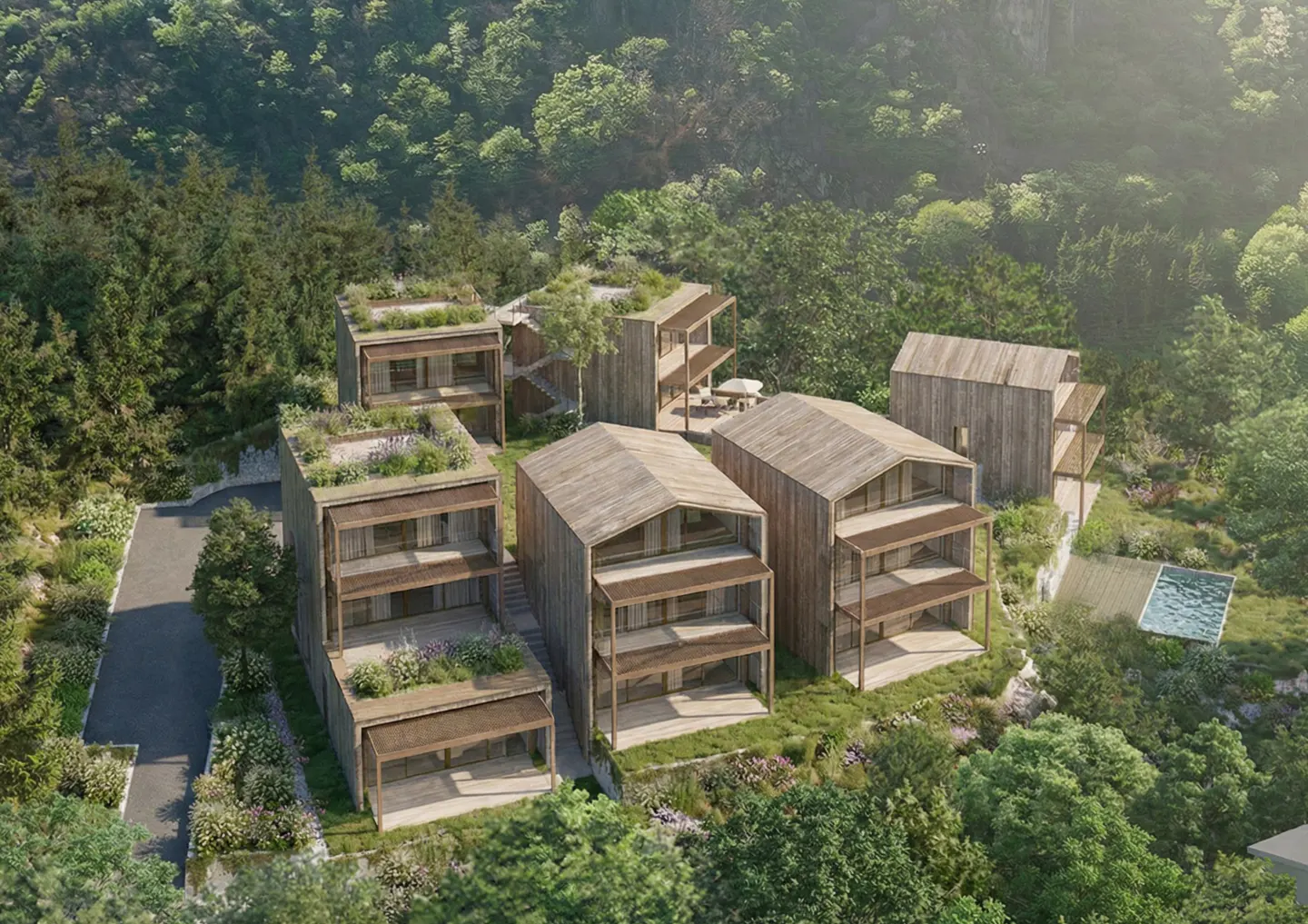 Aerial view of modern wooden houses with green roofs nestled in a lush forest setting. A pool is visible in the background.