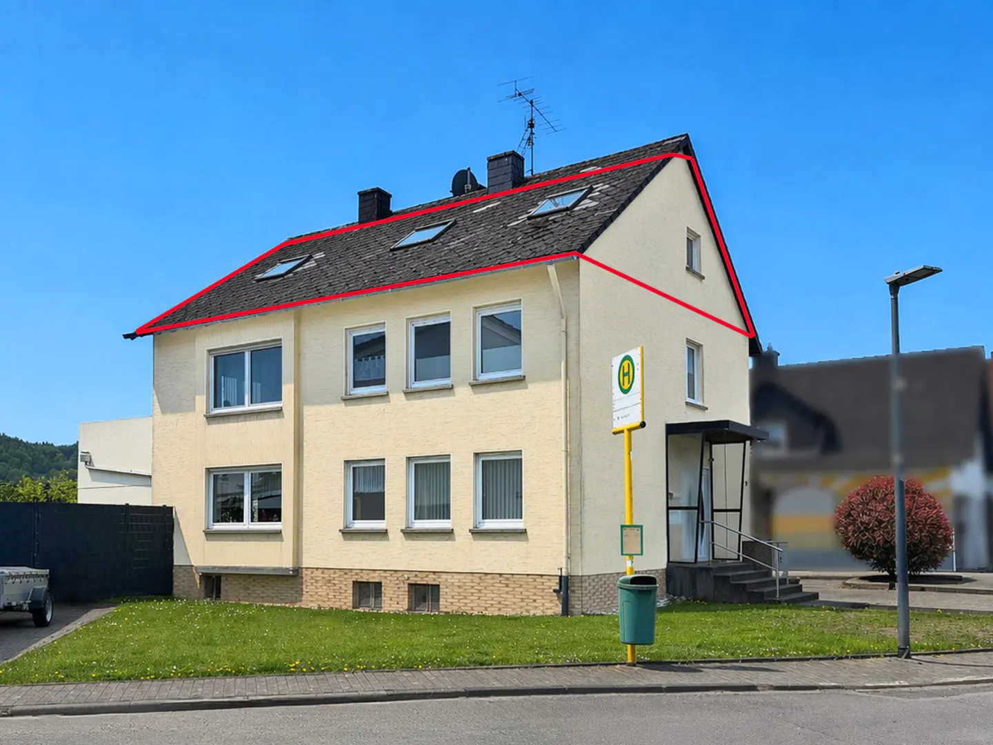 Two-story beige house with a red outline, a dark roof, and a bus stop sign in front.