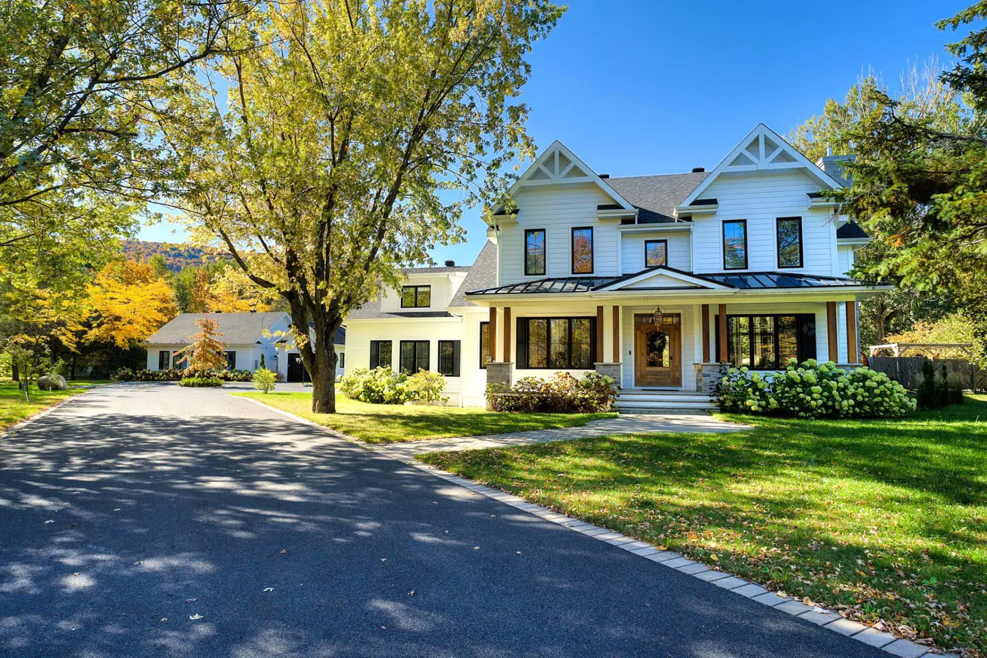 Two-story white house with black trim, a dark roof, and a long driveway on a sunny day.
