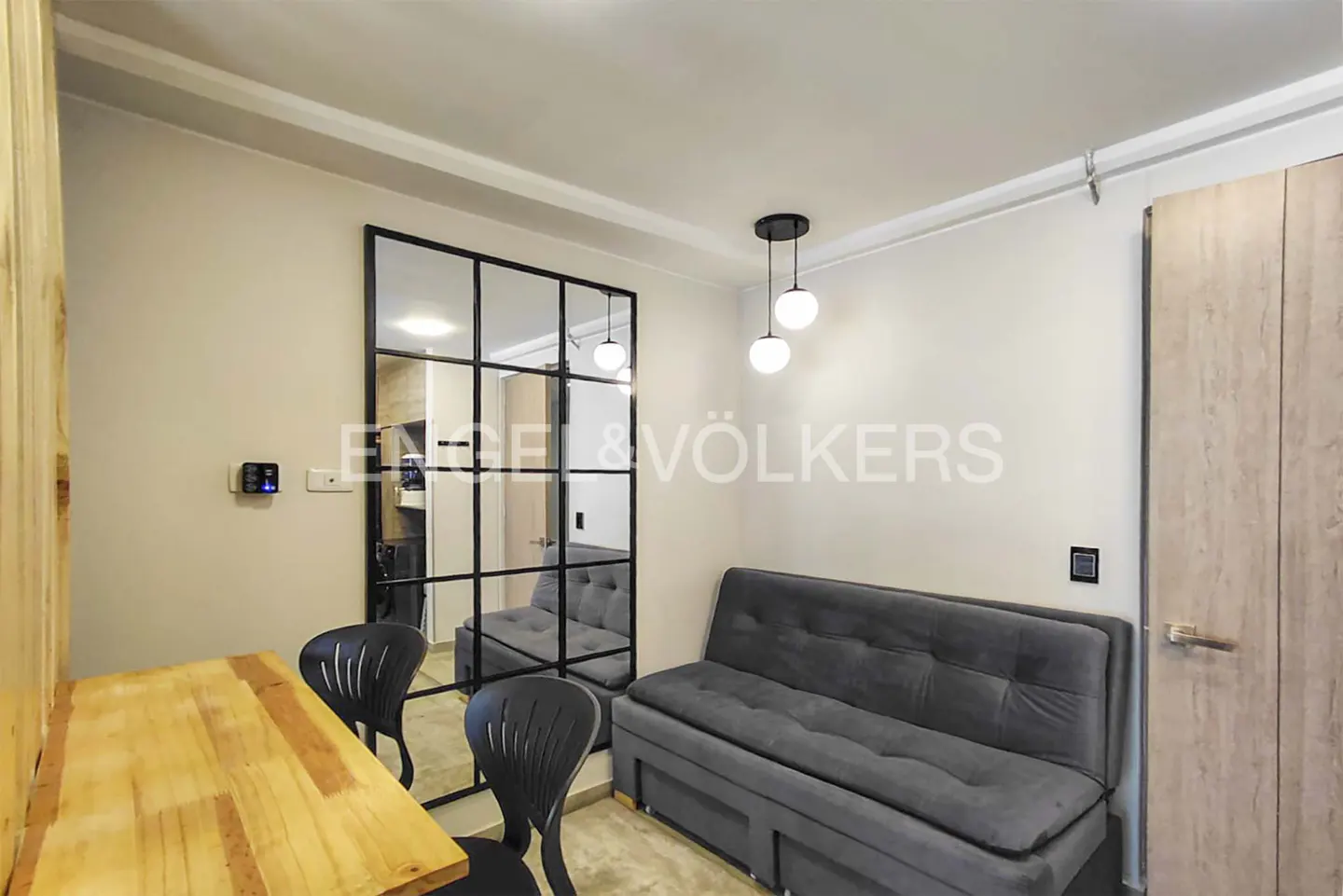 Living room with a wooden table, two black chairs, a gray sofa, and a black-framed mirror reflecting the room.