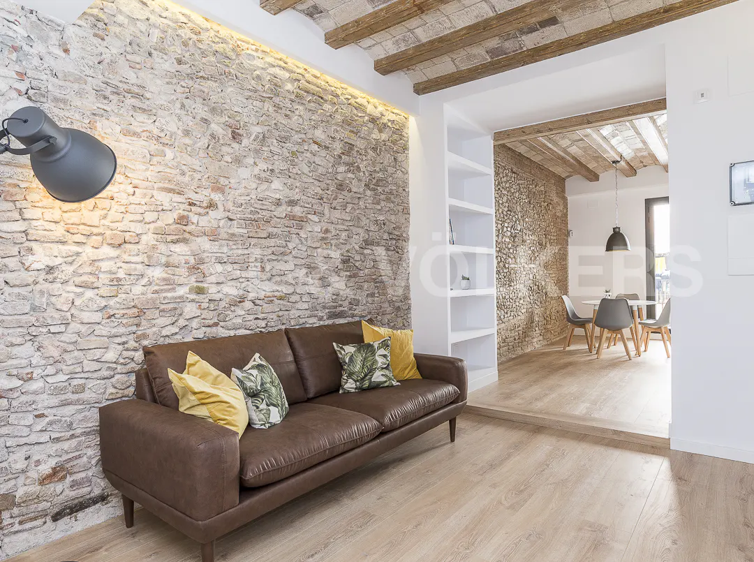 Brown leather sofa against a rustic brick wall in a modern living room with wood-beamed ceilings and a dining area.