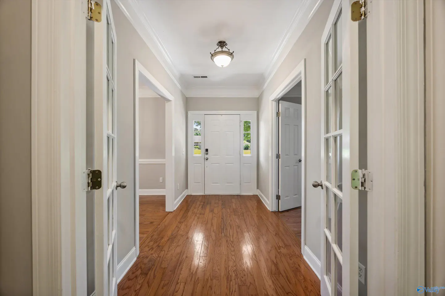 Bright foyer with hardwood floors, white trim, and a central light fixture leading to a white front door.