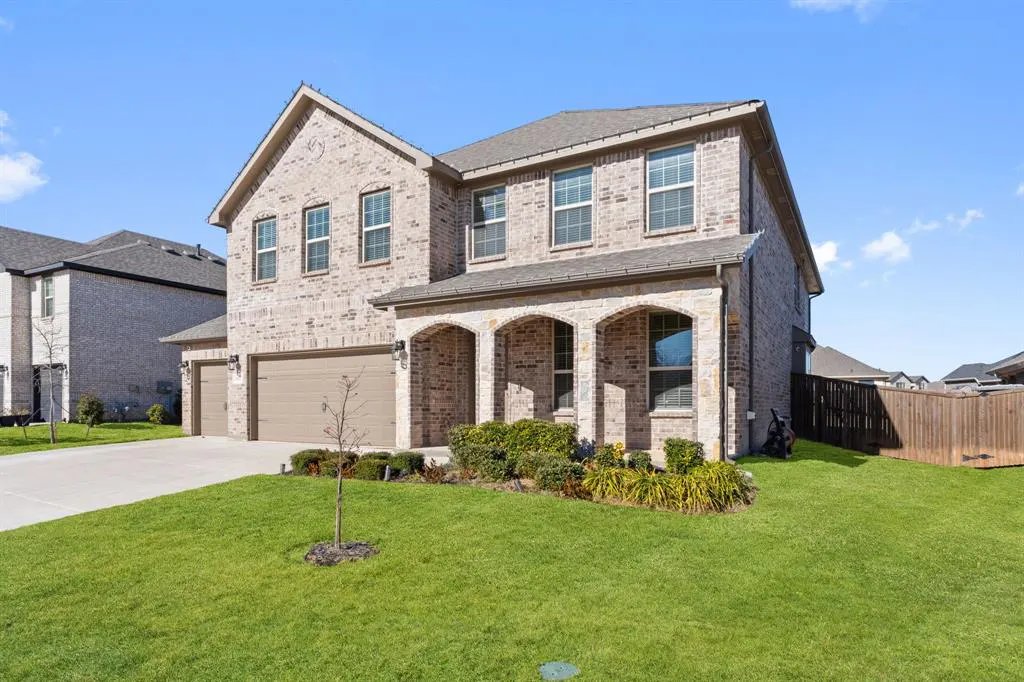 Two-story brick house with a three-car garage and arched porch. Green lawn and blue sky.
