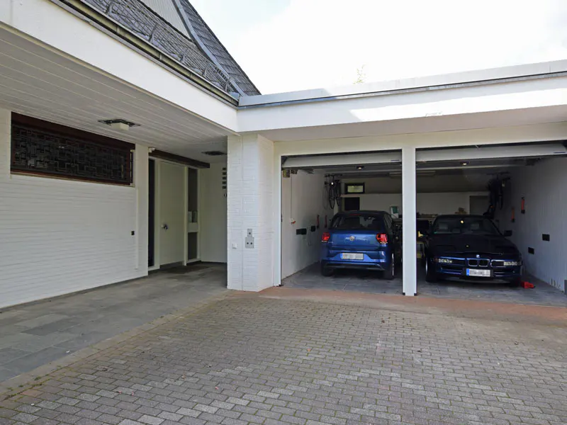 Two-car garage with a blue car in each bay. The exterior is white brick and the driveway is gray pavers.