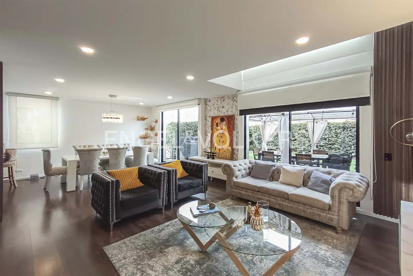 A bright, open living room with dark wood floors, a dining table, and a view of the backyard.