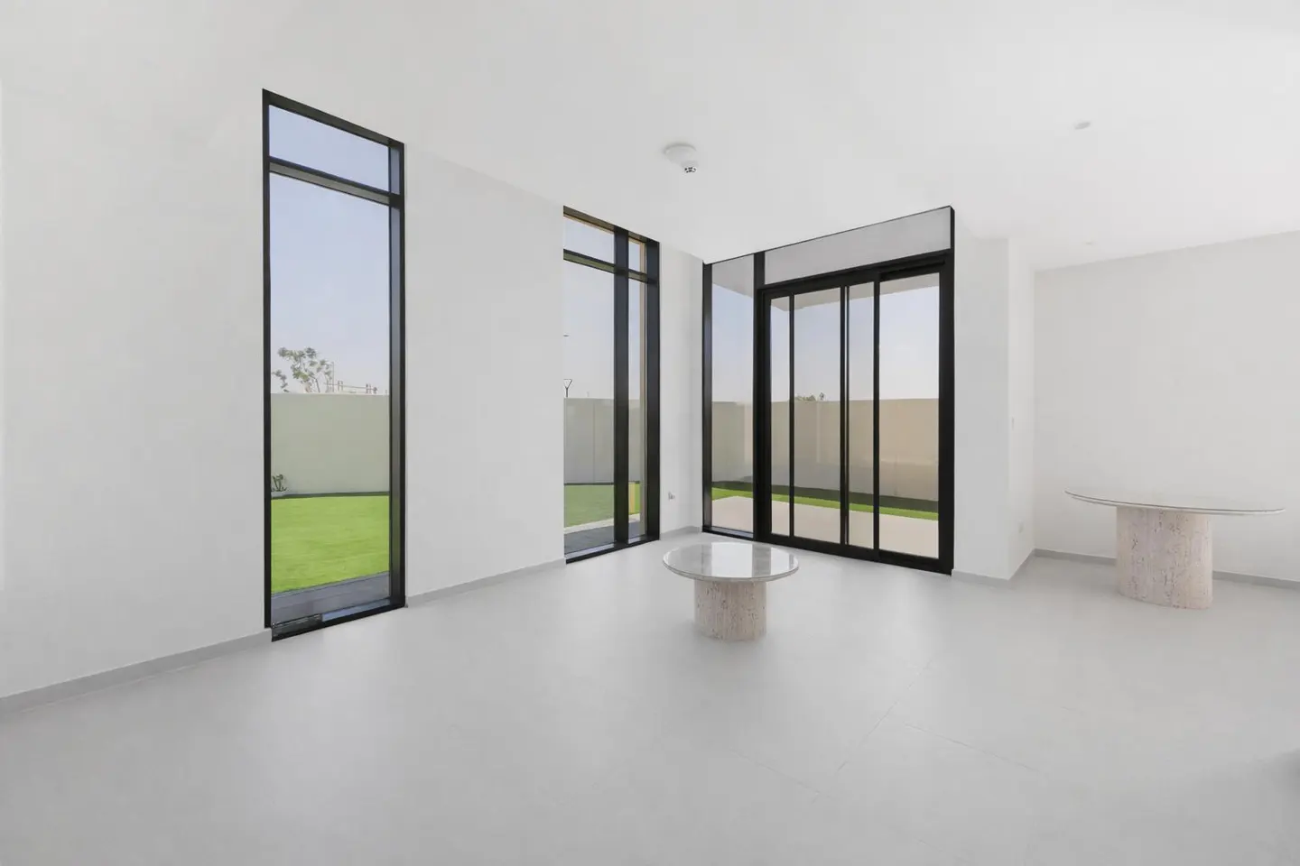 Minimalist room with white walls, light floors, floor-to-ceiling windows, and two stone-based glass tables.