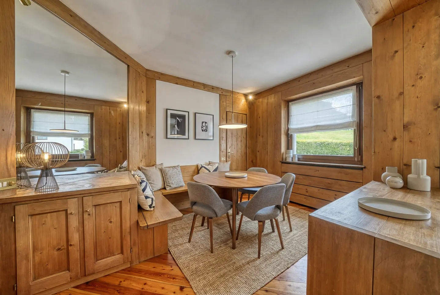 A cozy dining area with wood paneling, a round table with gray chairs, and a built-in bench with pillows.