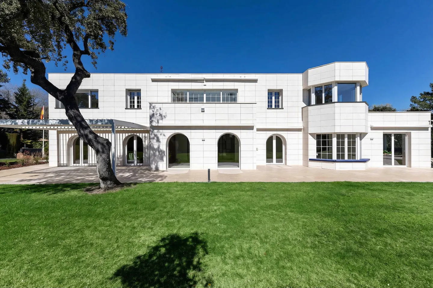 Exterior of a modern white stone house with arched doorways, windows, and a green lawn under a clear blue sky.