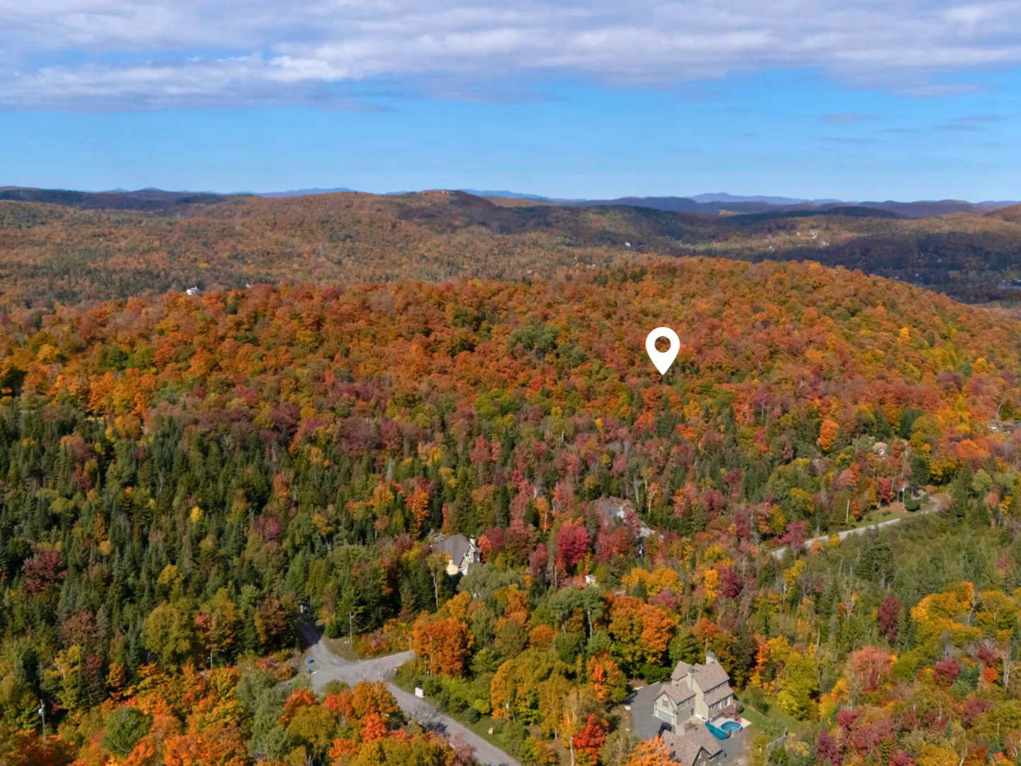 Aerial view of a wooded, hilly landscape in autumn colors with a white location pin.