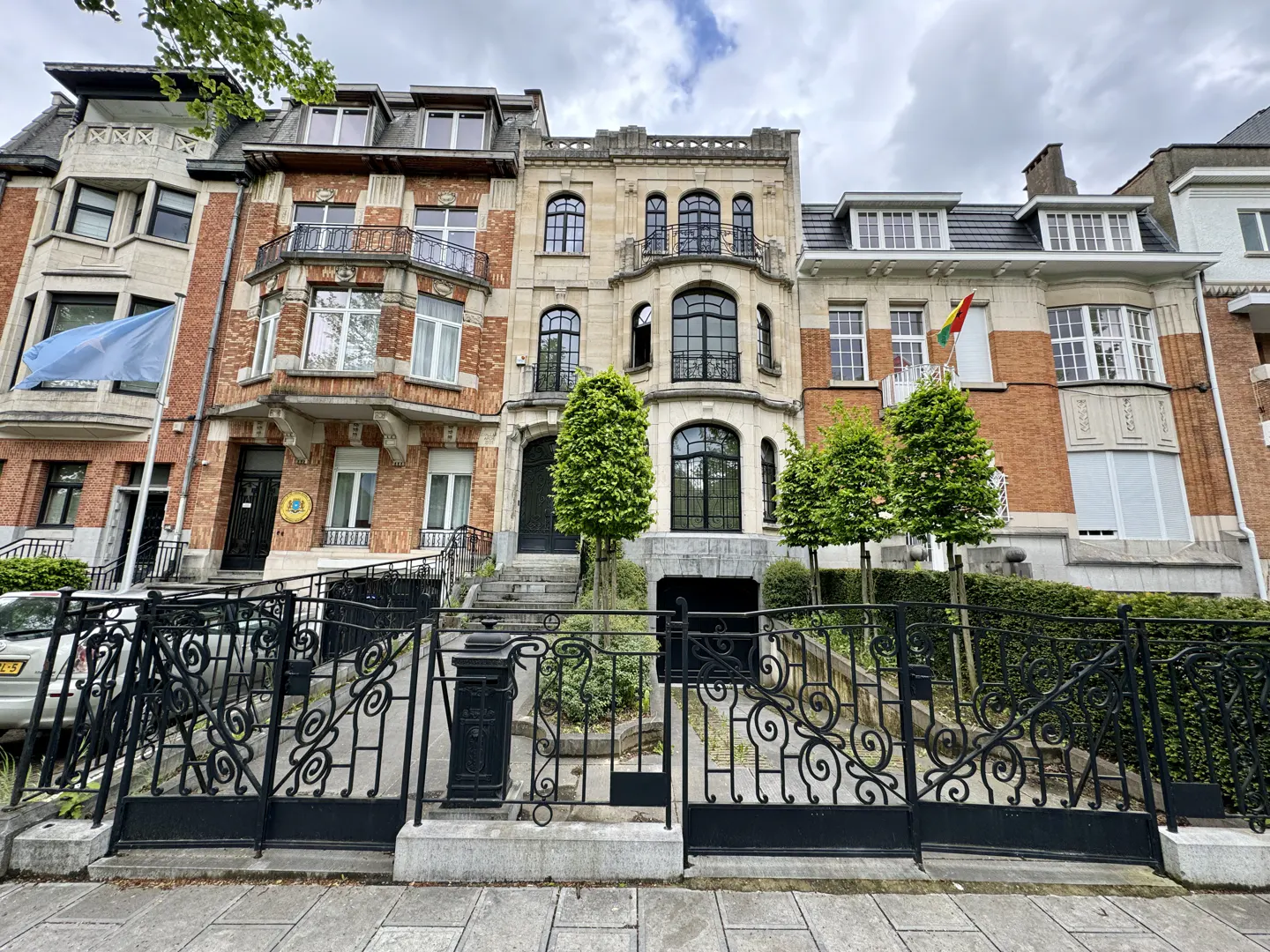Street view of four brick and stone townhouses behind a black wrought iron fence.