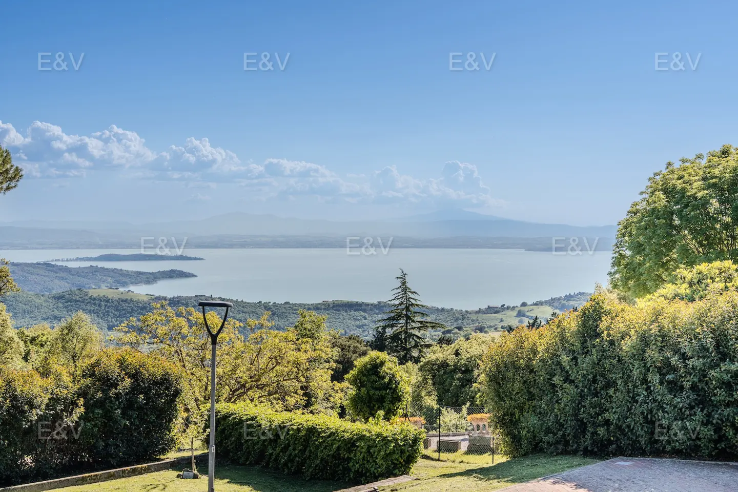 Scenic view of a lake surrounded by green hills and trees under a blue sky with white clouds.