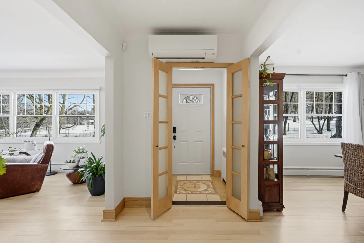 Bright foyer with open wood doors leading to a white front door. Living room and dining room visible.