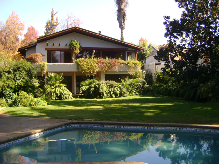 Two-story house with a pool. The house is surrounded by green grass and trees. The pool is in the foreground and reflects the house and trees.