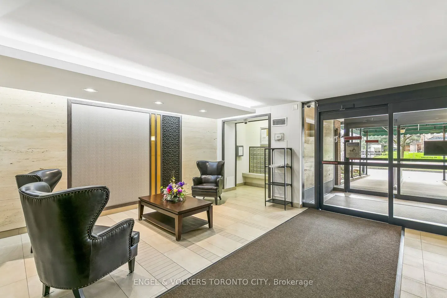 Lobby with two black leather chairs, a wood table with flowers, and a sliding glass door to the outside.