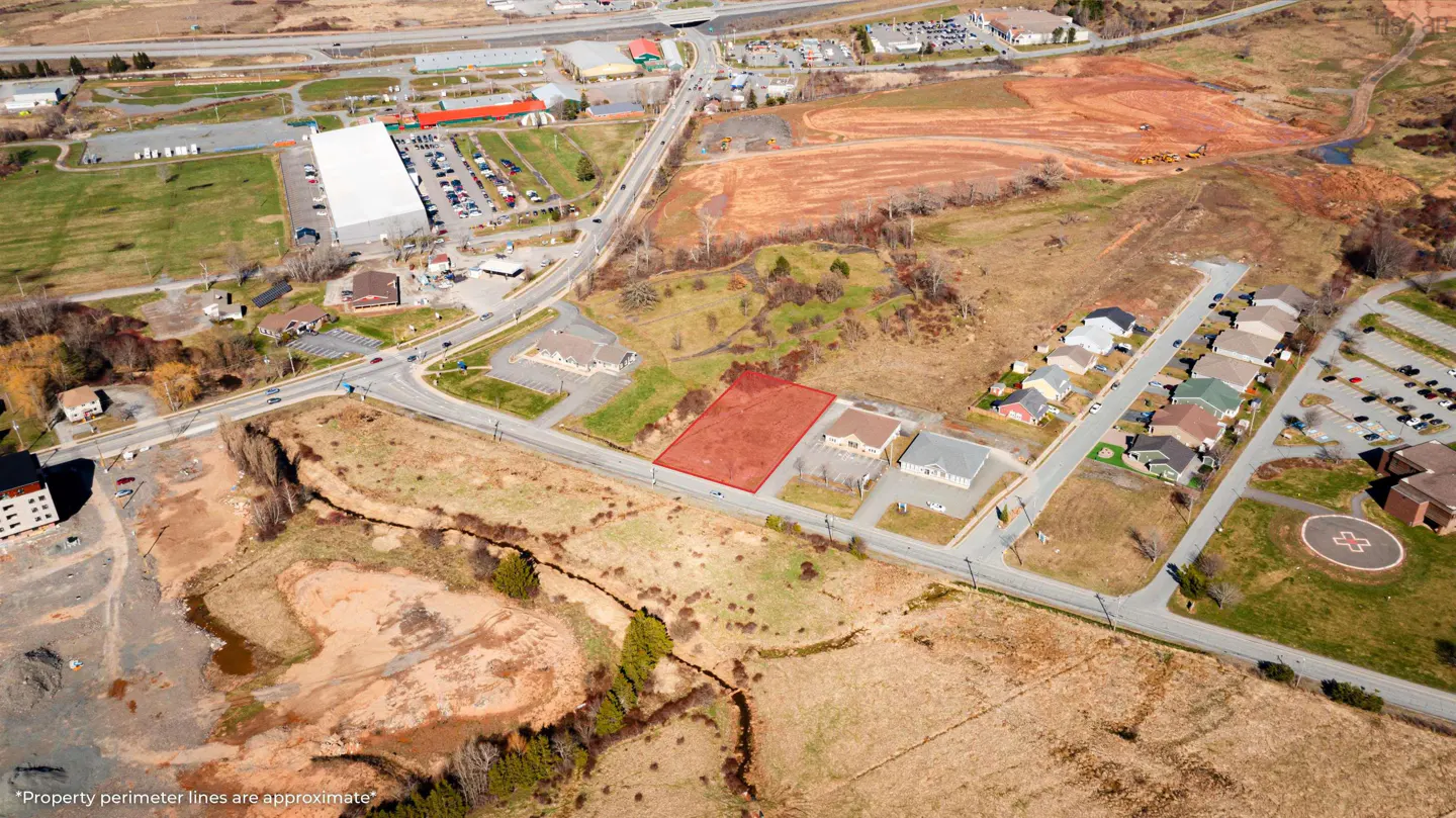 Aerial view of a vacant lot outlined in red, adjacent to commercial buildings and a residential area. Roads and a stream border the property.
