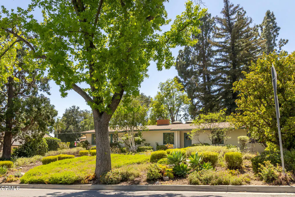 A single-story house with a green lawn and trees in front of it on a sunny day.