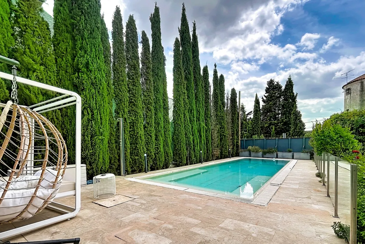 A backyard with a pool, tall green trees, and a hanging chair.