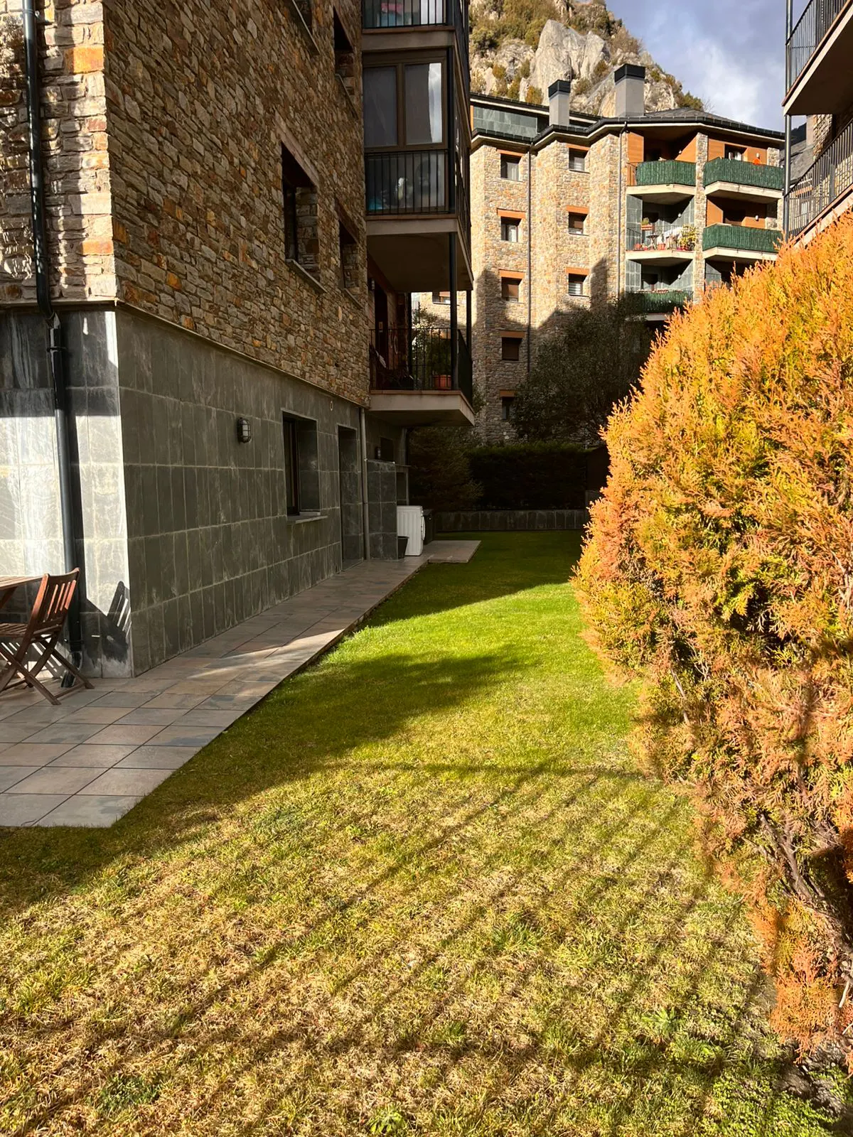 Exterior view of a stone apartment building with a green lawn and an orange bush.