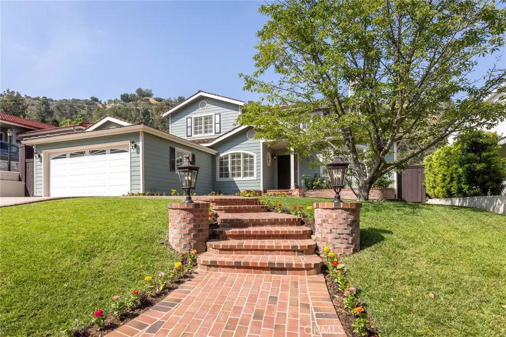 Exterior of a two-story blue house with a brick walkway and steps leading to the front door. A large tree is in the front yard.