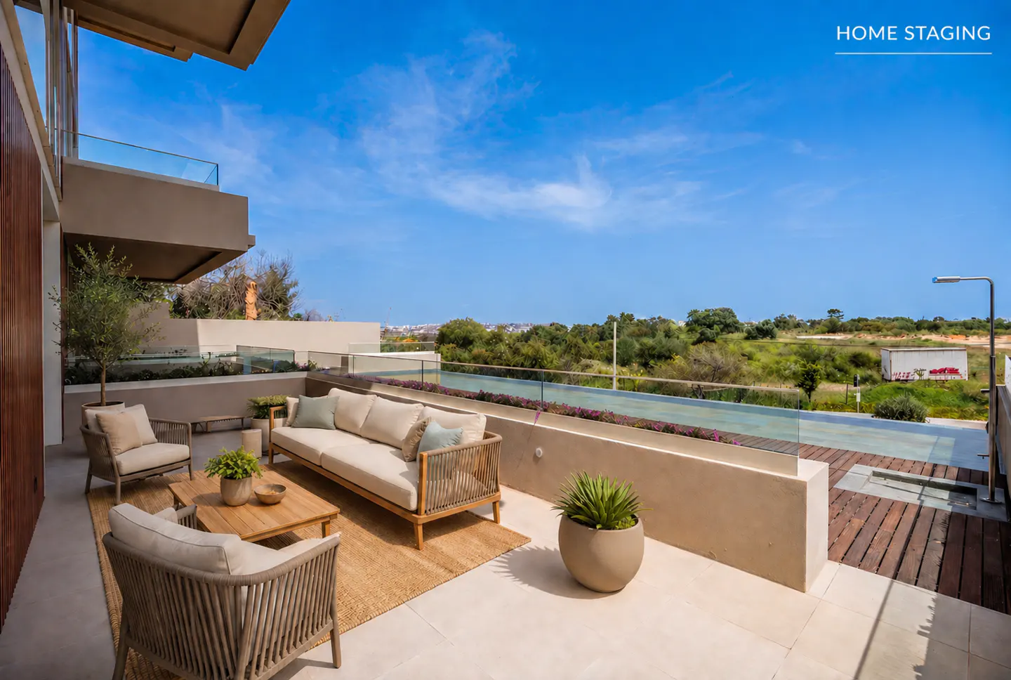 Outdoor patio with beige furniture set, including a sofa, chairs, and a wooden coffee table on a jute rug, overlooking a green landscape.