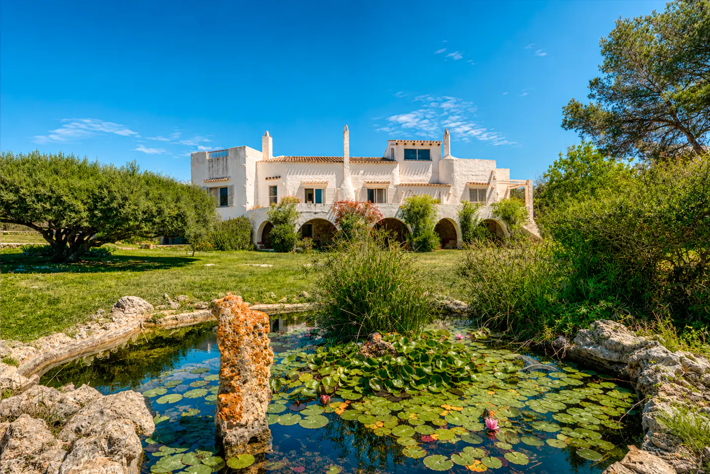 Exterior view of a white villa with a pond filled with lily pads in the foreground.