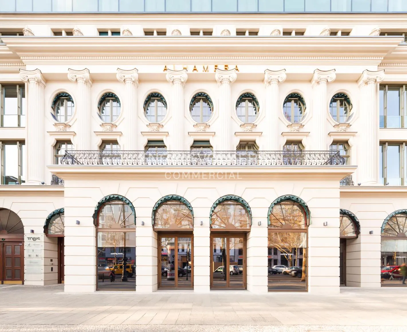 Exterior of a white commercial building with arched windows and doors. Balcony with black railing. "ALHAMBRA COMMERCIAL" is written on the building.