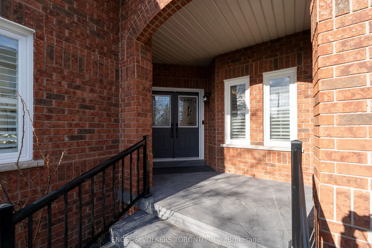 Brick house entrance with black double doors, white framed windows, and black railings leading to a gray porch.