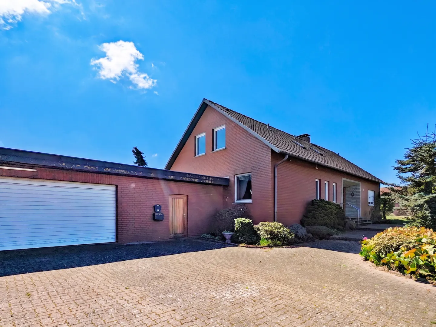 Exterior view of a red brick house with a garage and a paved driveway under a blue sky.