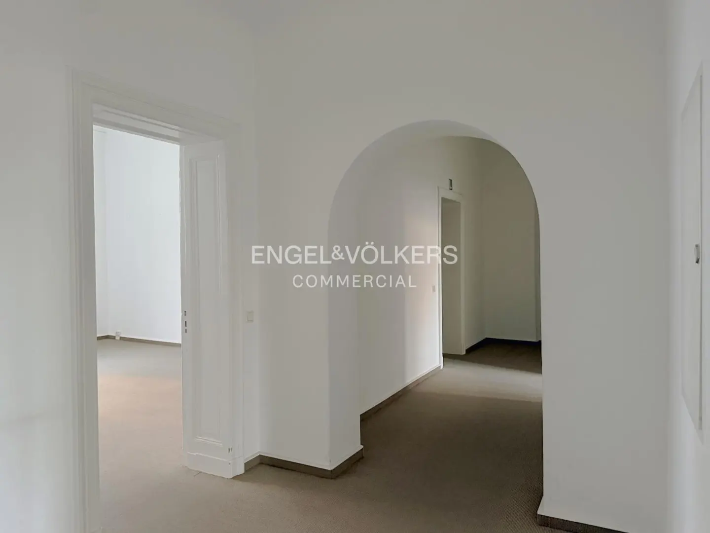 Interior view of a white-walled commercial space with doorways and an arched opening. The floor is carpeted in a neutral tone.