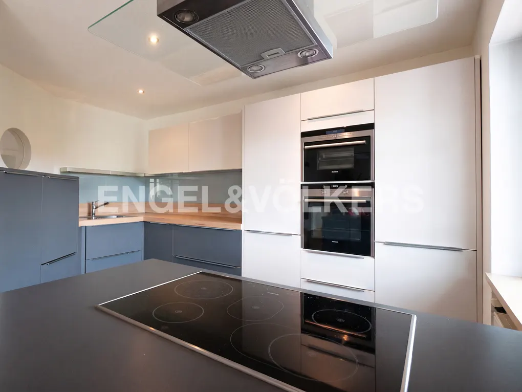 Modern kitchen with white and grey cabinets, a black induction cooktop on an island, and built-in stainless steel ovens.