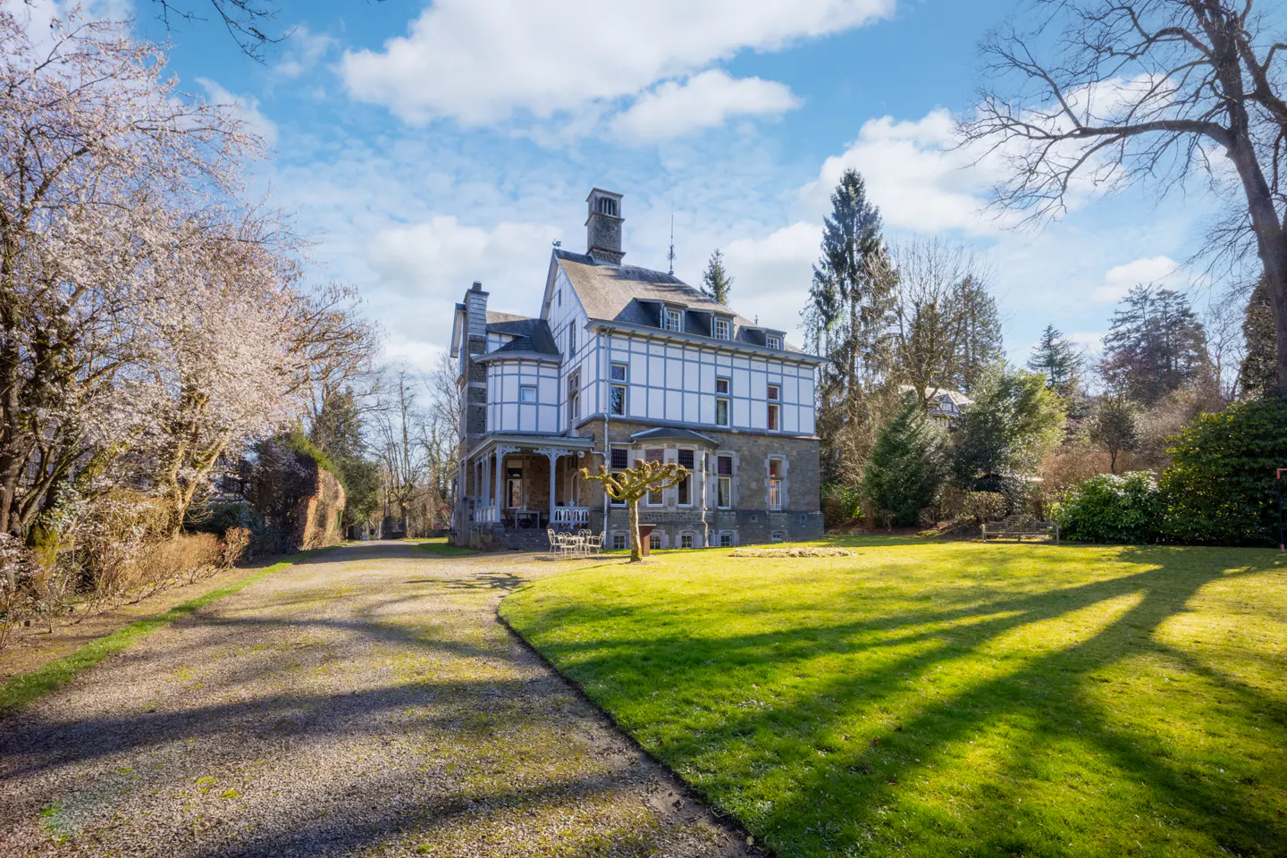 Exterior view of a large, two-story white house with a gray roof, stone foundation, and green lawn under a blue sky with clouds.