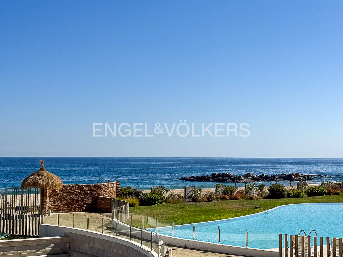 Ocean view from a property with a pool. Blue sky, water, and green grass. Engel & Völkers logo.