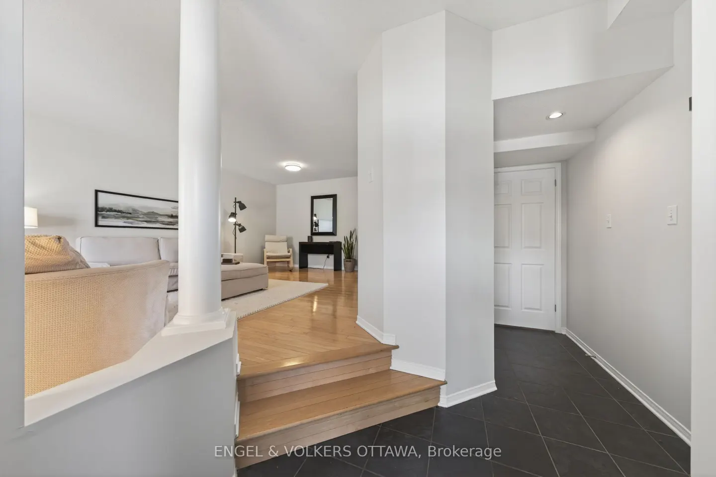 Interior view of a home with hardwood floors, white walls, and a column separating the living room from the hallway.