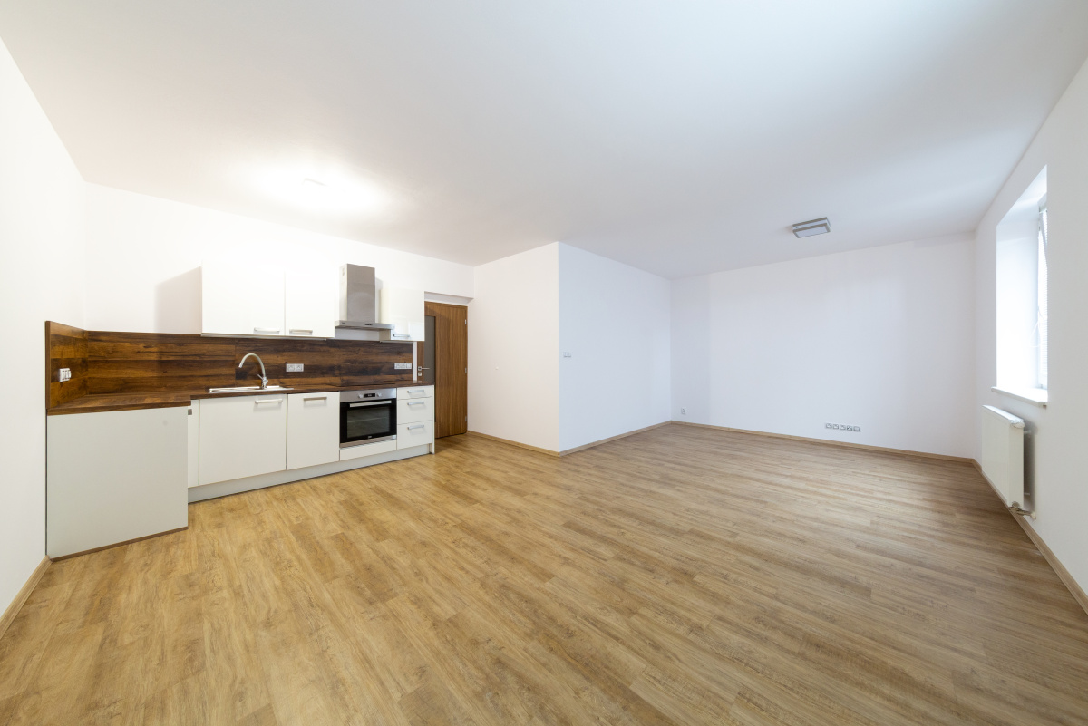 Modern open-plan kitchen with white cabinets, dark wood backsplash, and light wood flooring in a bright, empty room. [AI-generated text]