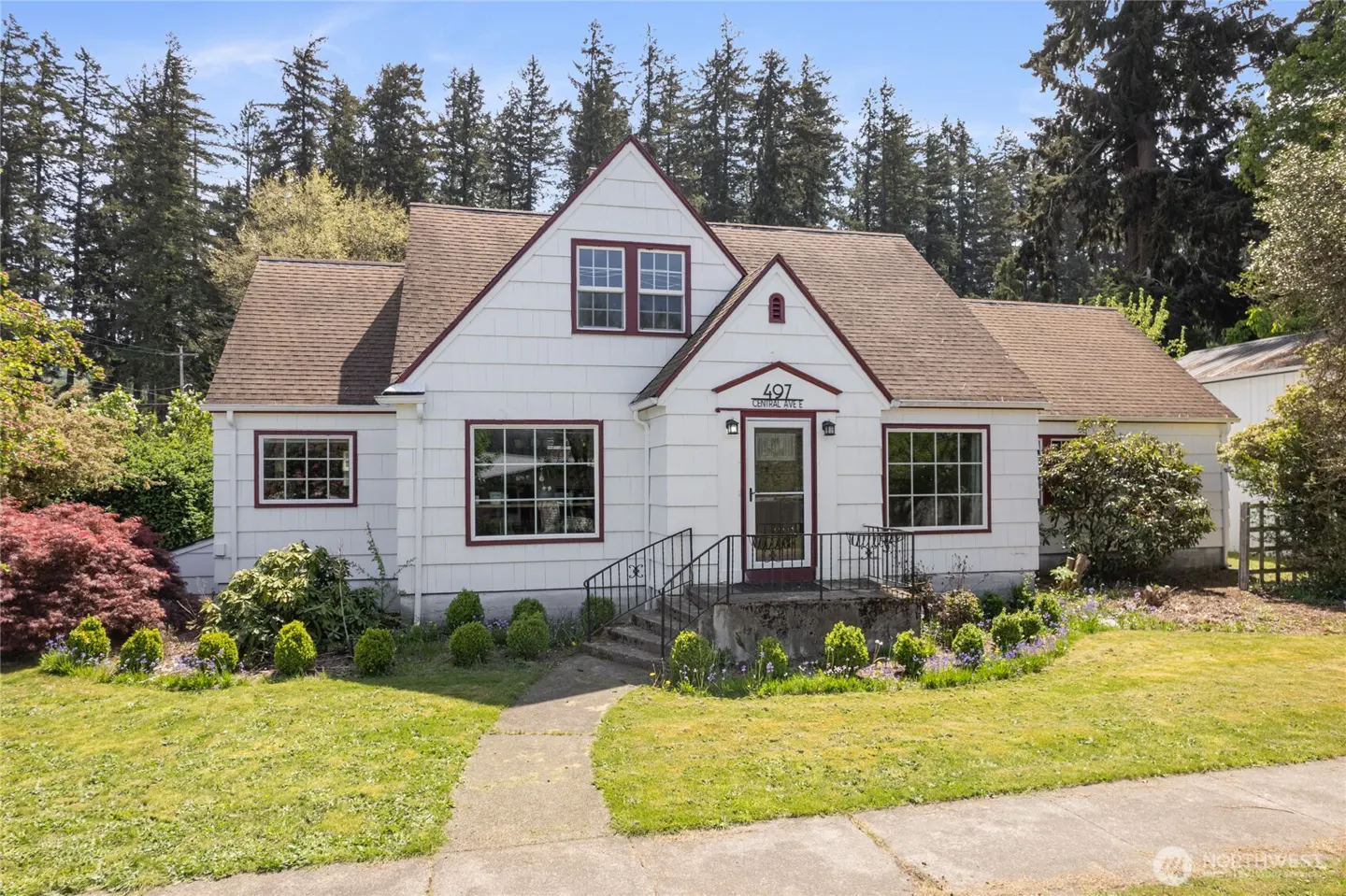White house with brown roof and trim, number 497 above the door, surrounded by green lawn and trees.