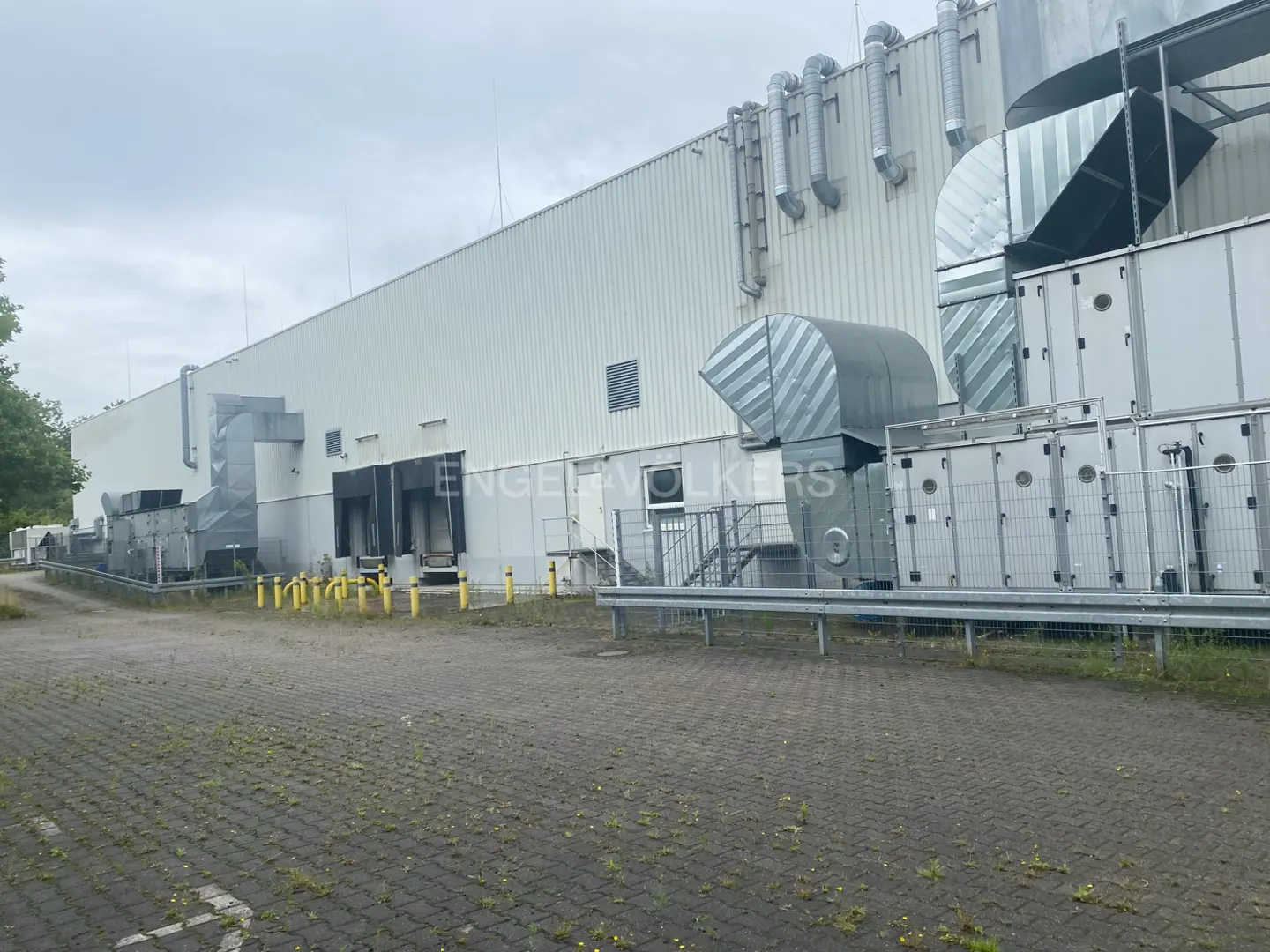 Exterior view of a large, white industrial building with loading docks and ventilation systems on a cloudy day.