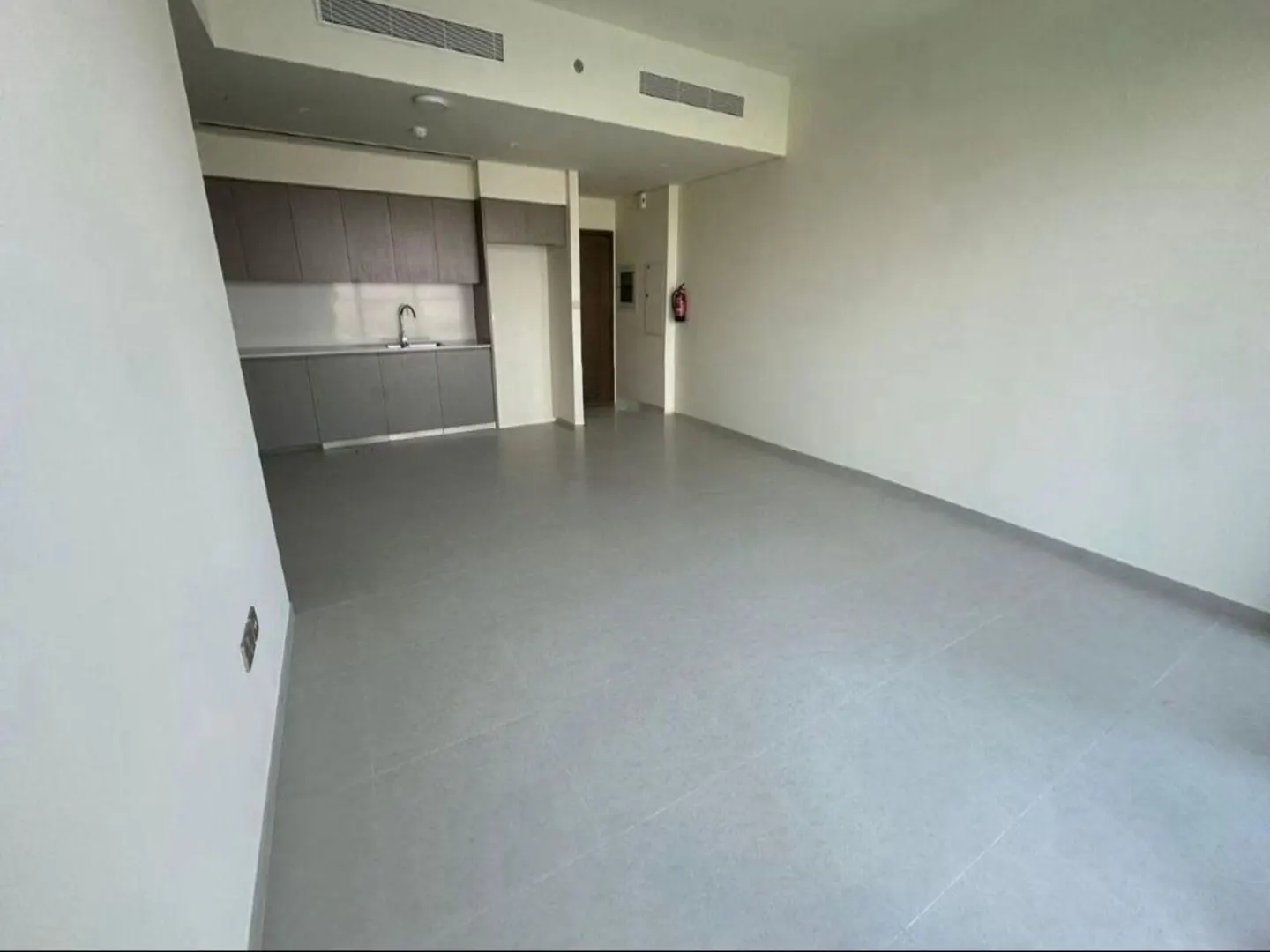 An empty apartment with gray tile flooring, white walls, and a gray kitchen with a sink. A doorway is visible in the background.