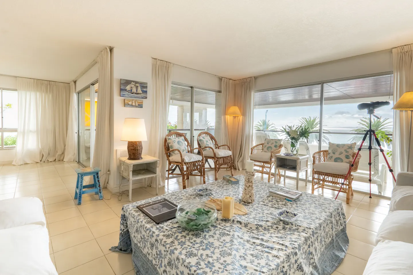 Bright living room with wicker chairs, a blue floral tablecloth, and a telescope overlooking the ocean.