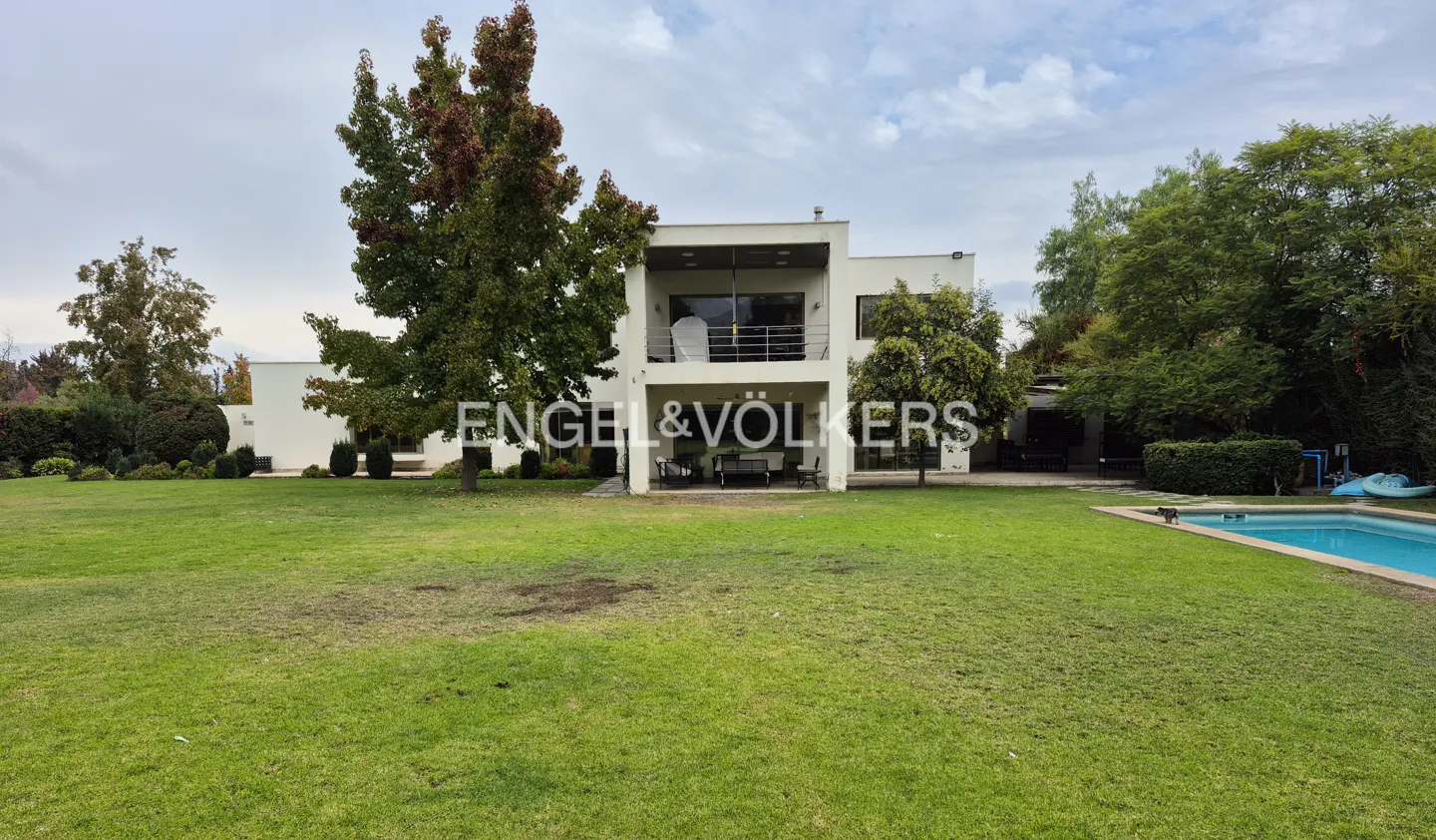 Two-story white house with a balcony, a large green lawn, trees, and a blue swimming pool.