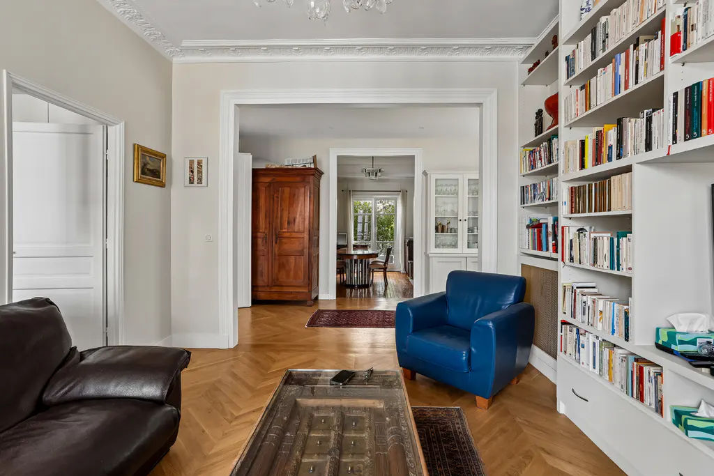 A living room with a brown leather sofa, blue armchair, and a bookshelf filled with books.